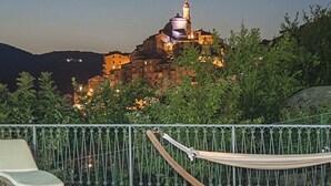 A hammock on a terrace with a pool and a view of a historic building at dusk.