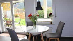 A dining area with a round table, two grey chairs, a vase with flowers, and a black pendant light.