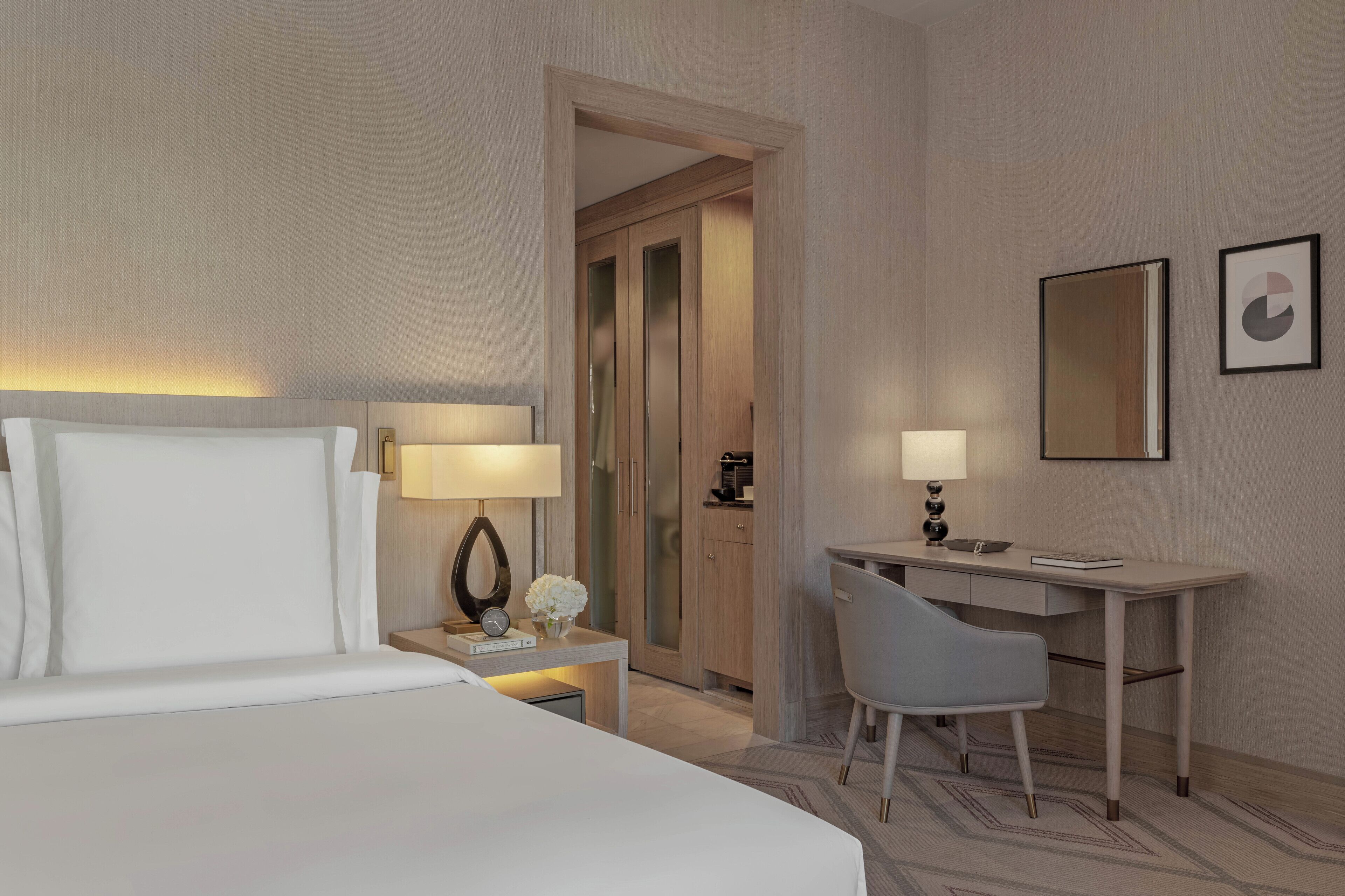 A hotel room with a bed, bedside table, lamp, desk, chair, and a mirror.