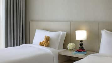 A hotel room with a bed, a nightstand, a lamp, a teddy bear, and a vase with flowers.