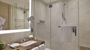 Un baño moderno con ducha de vidrio, tocador de madera con lavamanos y un espejo grande.
