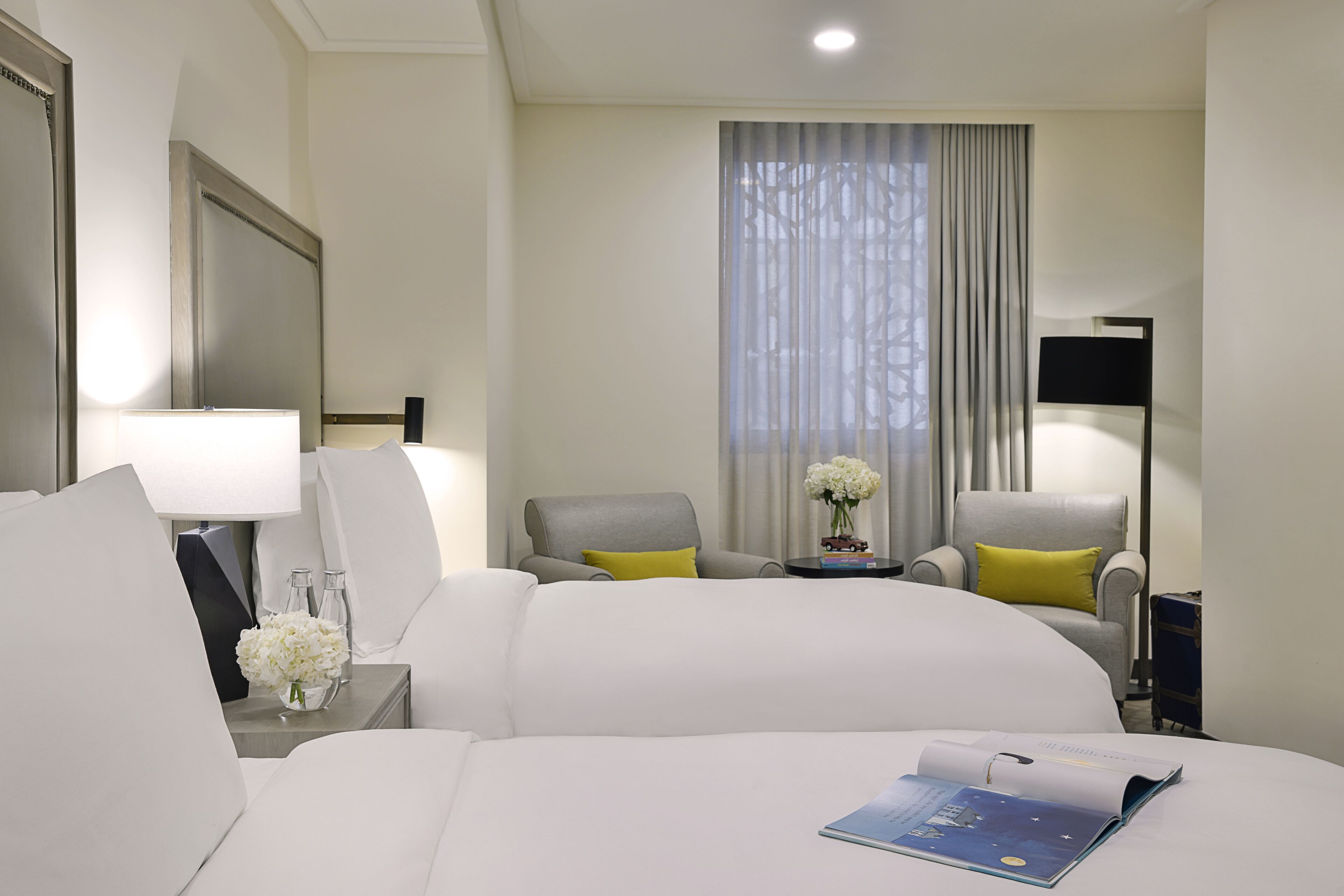 Una habitación de hotel con una cama grande, dos sillones, una mesita con un jarrón de flores y una lámpara.
