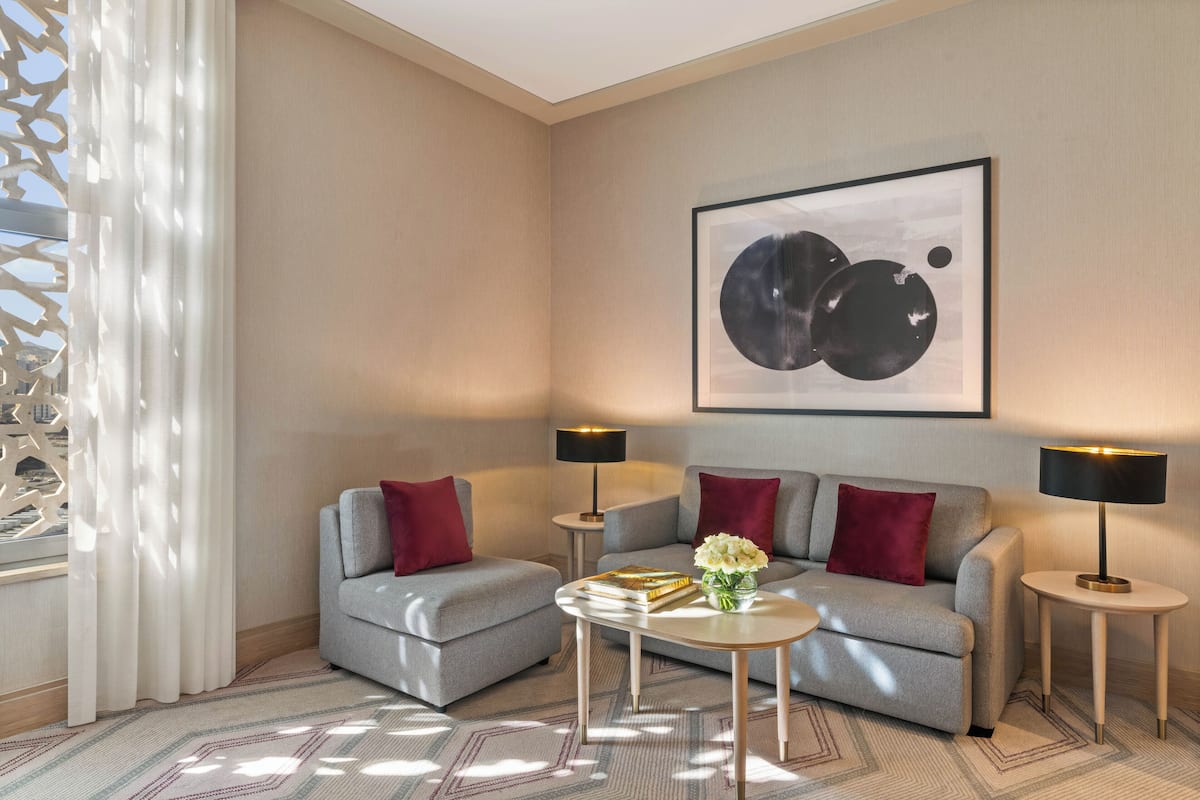 A modern living room with two grey sofas, red cushions, a round coffee table with books and flowers, two side tables with lamps, and a large abstract painting on the wall.