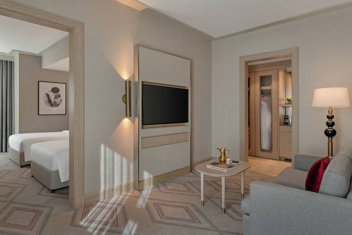 A hotel room with a bed, a TV, a small table with a lamp, and a sofa.