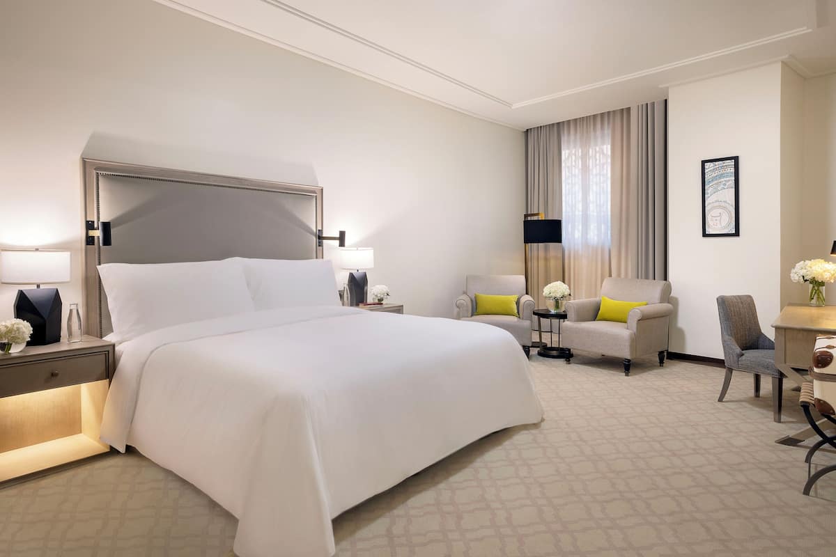 A hotel room with a large bed, a desk, a chair, and a sofa.