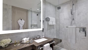 A modern bathroom with a large mirror, a wooden vanity, a glass shower enclosure, and marble walls.