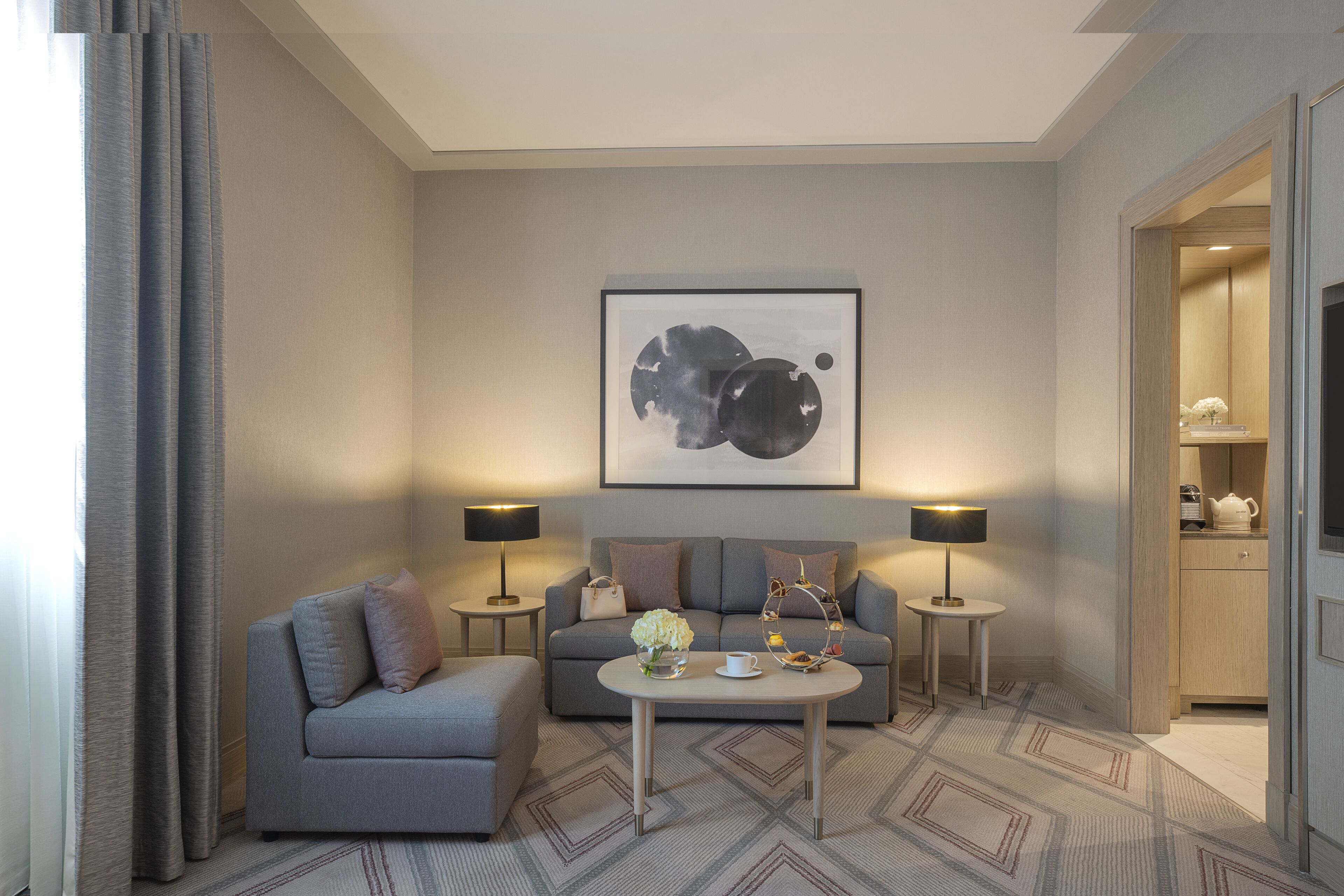 Een moderne woonkamer met een grijze bank, twee bijzettafels, een salontafel en een ingelijst abstract kunstwerk aan de muur.