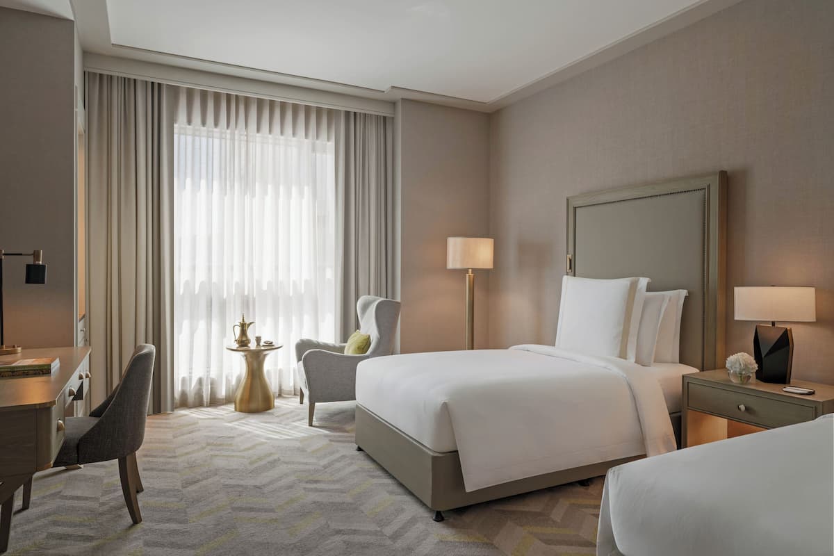 A hotel room with a large bed, a desk, a chair, a nightstand, and a lamp.