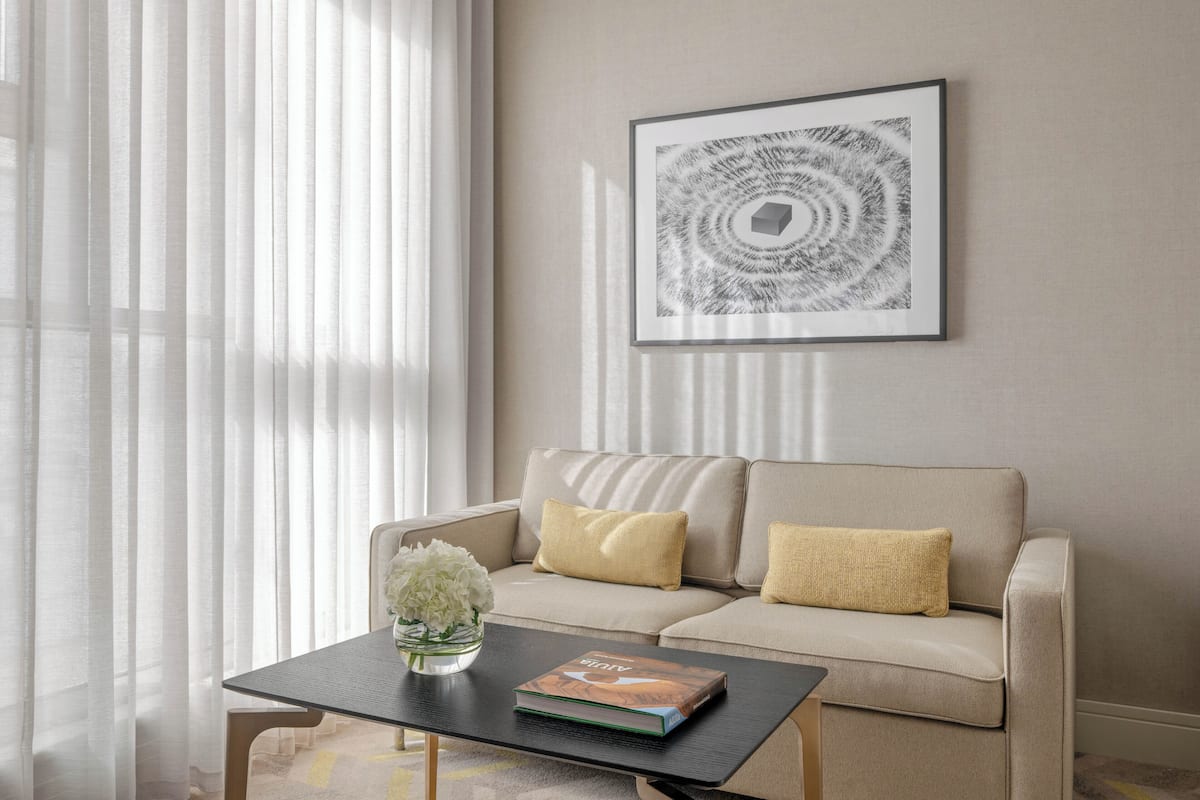 A modern living room with a beige sofa, a black coffee table, and a framed abstract artwork on the wall.