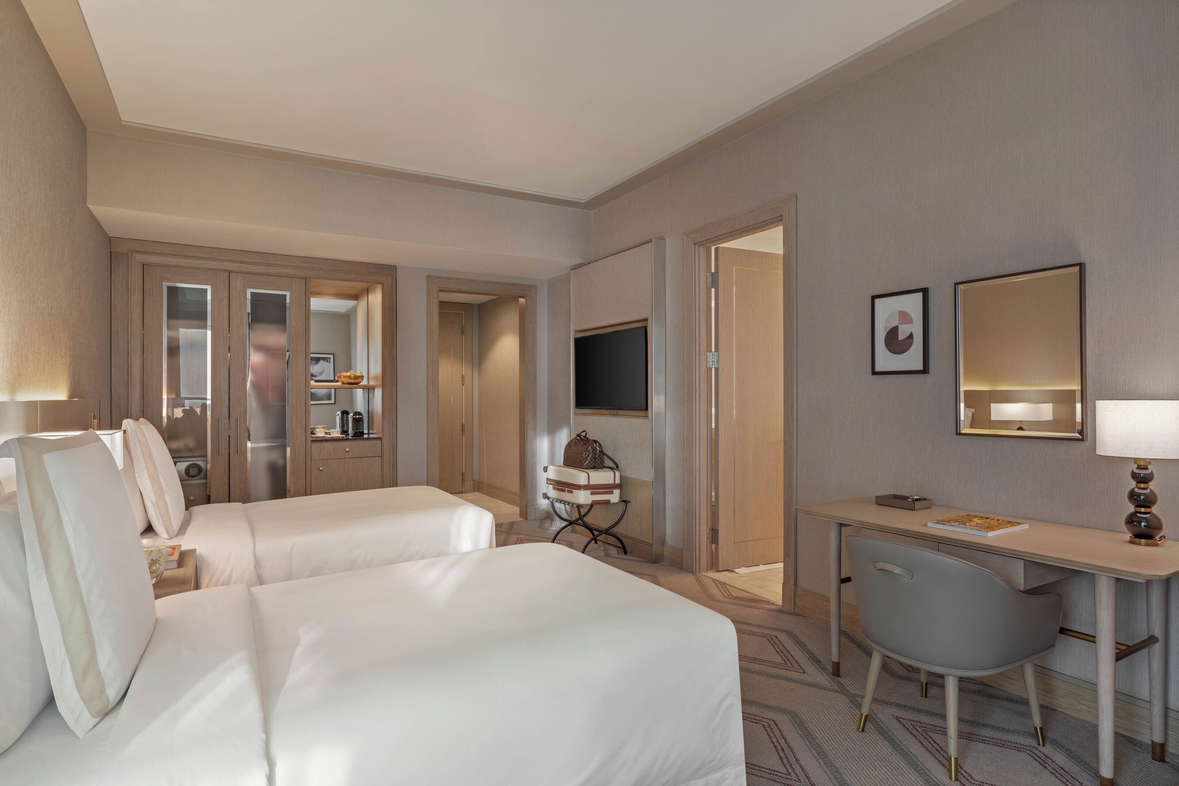 A hotel room with two beds, a desk, a chair, a television, and a mirror.