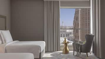 A hotel room with a bed, a chair, a small table, and a large window offering a city view.