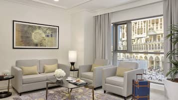 A modern hotel room with a sofa set, a coffee table, a lamp, a view of a historic building, and a suitcase.