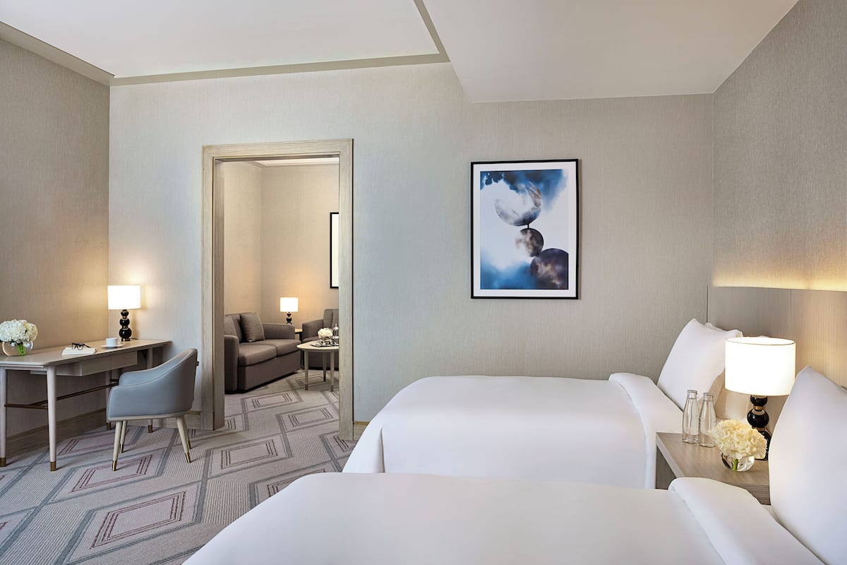 A hotel room with two beds, a desk, a chair, a sofa, and a framed picture on the wall.