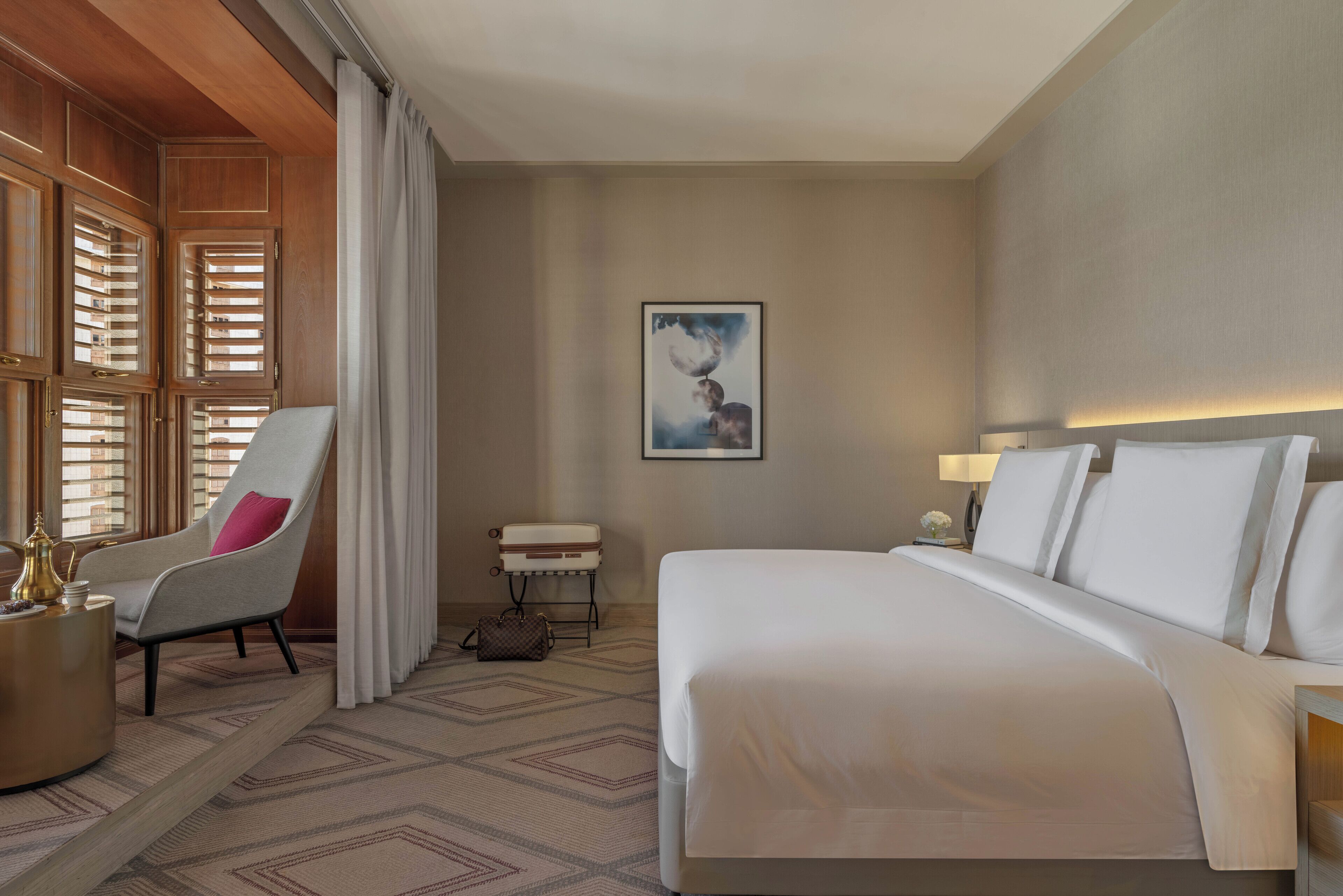 Habitación de hotel con una cama grande, una silla, una mesita y un cuadro colgado en la pared.