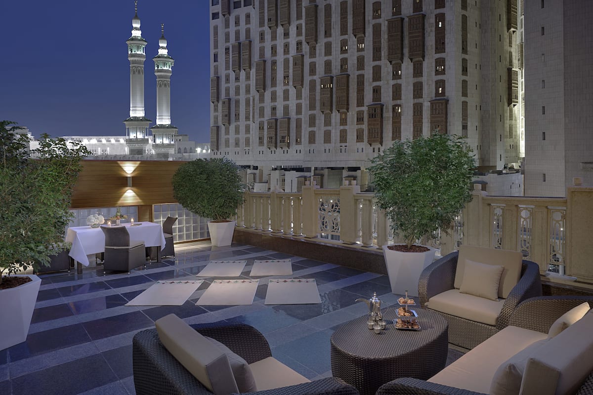 A rooftop lounge with outdoor seating, potted plants, and a view of a tall building with minarets.
