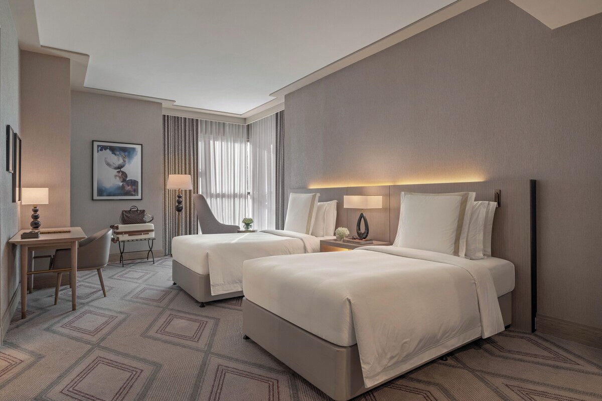 Ein Hotelzimmer mit zwei Betten, einem Schreibtisch, einem Stuhl und einem kleinen Tisch.