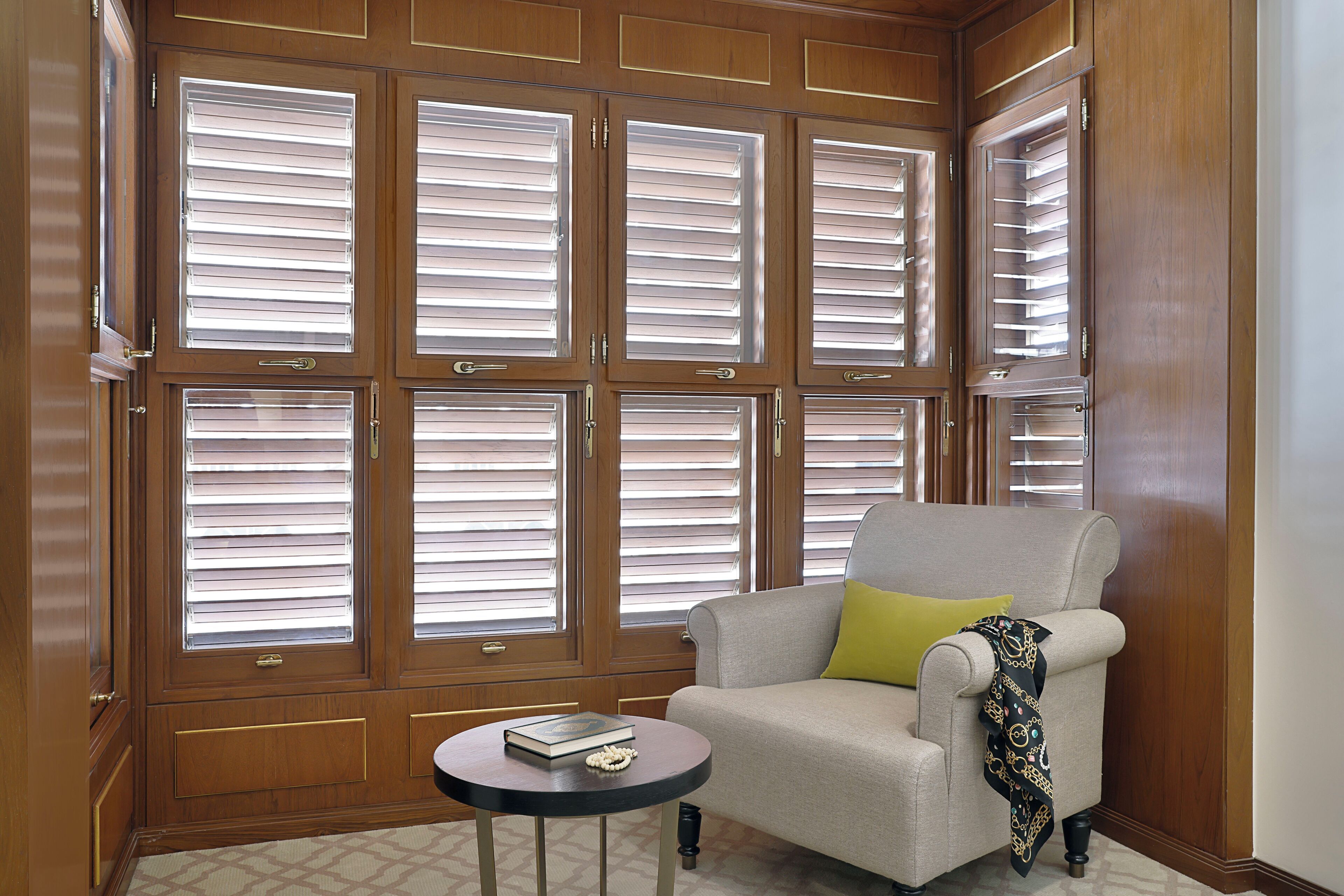 A room with a large window with blinds, a sofa with a yellow pillow, and a small table with a book and decorative item.
