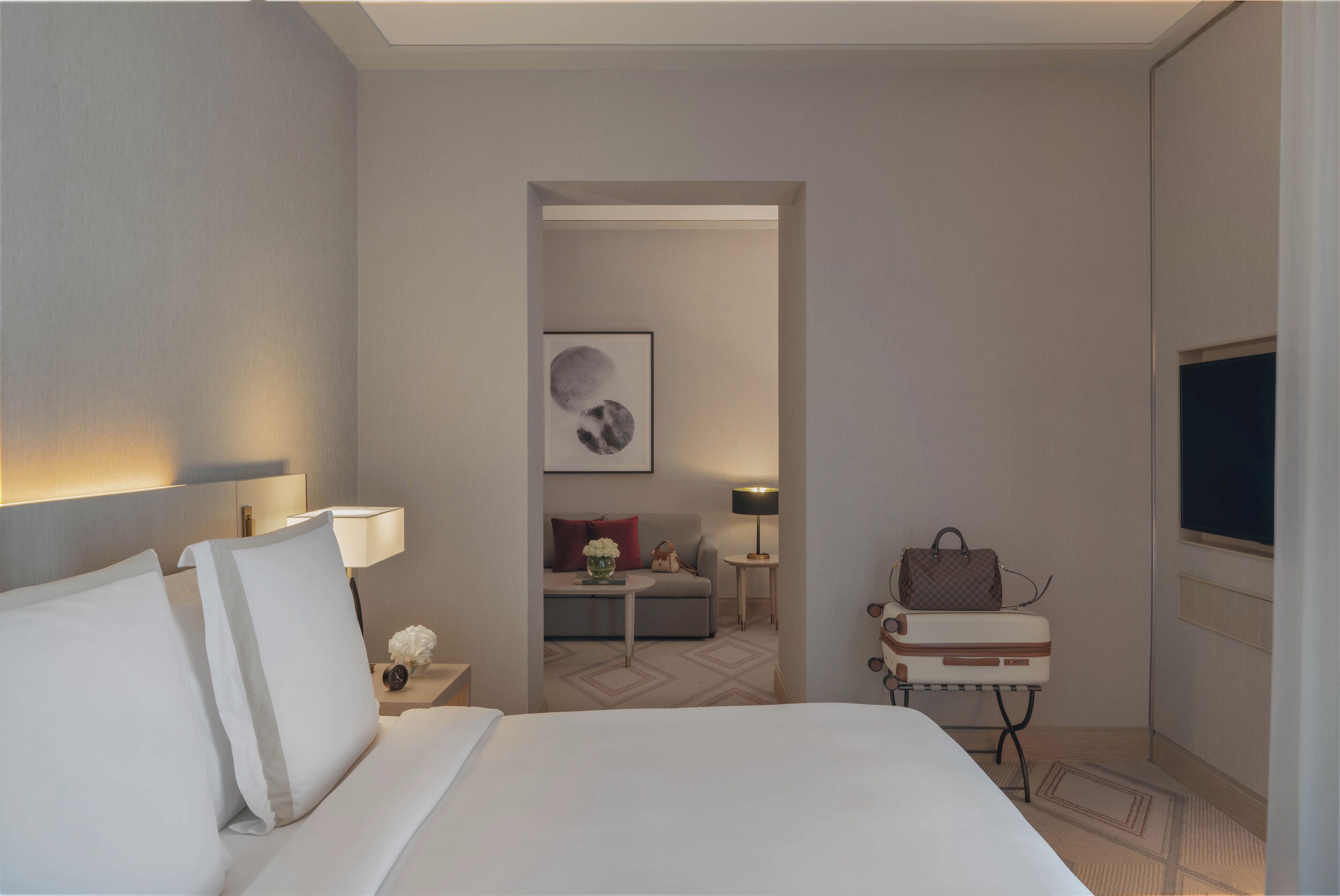 Habitación de hotel con una cama grande, televisión, escritorio con lámpara, sofá y una mesita con un florero.