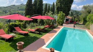 Una piscina con sombrillas rojas, tumbonas y vistas a colinas verdes.