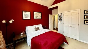 A bedroom with a red wall, white bed, and a ceiling fan. There are framed pictures on the wall and a door with a mirror. - Perfect luxury home, close to social settings but far enough for peace. (Acworth)