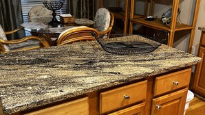 A kitchen with wooden cabinets, a granite countertop, and a dining area with wicker chairs and a table. - Perfect luxury home, close to social settings but far enough for peace. (Acworth)