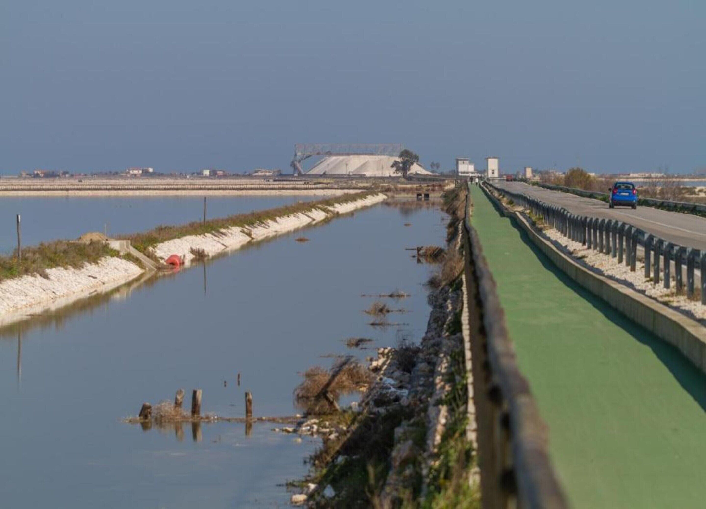 A highway with a green barrier and a body of water on one side.