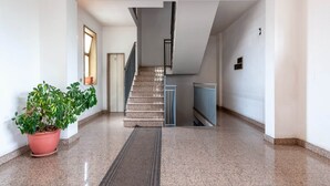 Un pasillo limpio y moderno con una escalera que lleva a un piso superior. Se ve una planta en maceta a la izquierda, y una puerta a la derecha.