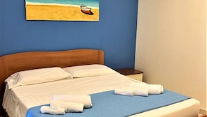 Uma cama com lençóis brancos, um cobertor azul e duas toalhas sobre a cama.