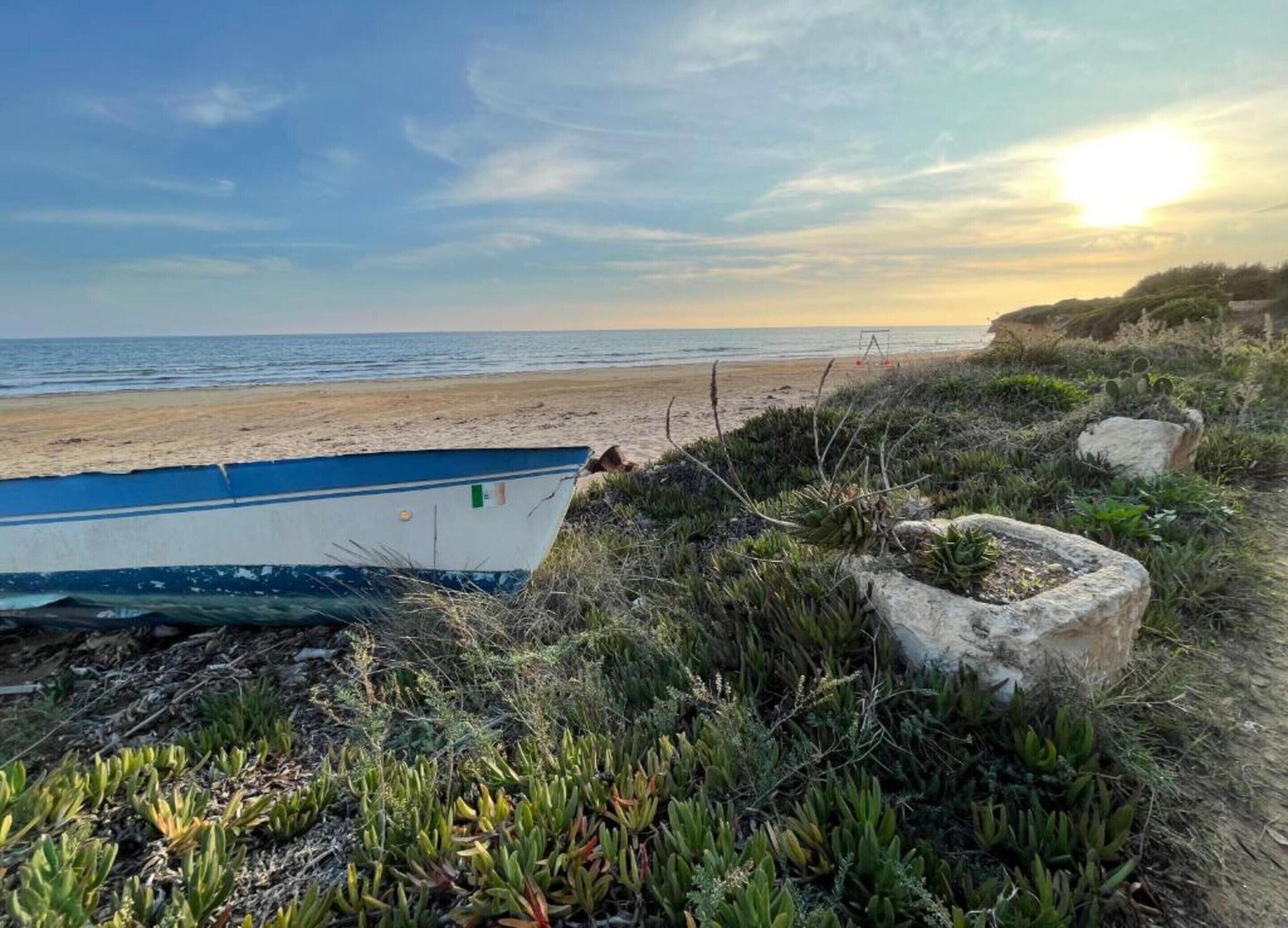 A boat on a beach with a clear sky and the sun setting in the background.