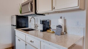 Cocina compacta con pileta, microondas, cafetera y un rollo de toallas de papel.