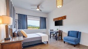 Una habitación de hotel con cama, escritorio, silla, televisor y ventana con cortinas.
