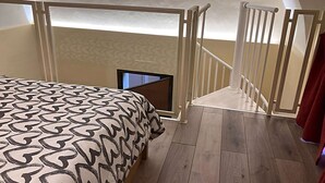 Een slaapkamer met een bed met een patroondraad, een kleine televisie en een houten vloer.