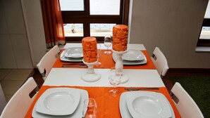 A dining table set with white plates, silverware, and wine glasses, centered on an orange table runner with a view of the outdoors through large windows. - Estúdio vista rio Douro (Vila Nova de Gaia)
