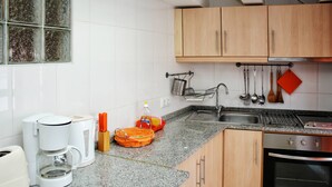 A kitchen with wooden cabinets, a stainless steel oven, a coffee maker, and a sink. - Estúdio vista rio Douro (Vila Nova de Gaia)