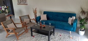 A living room with a blue sofa, two wooden chairs, a coffee table, and a small table with a vase and fruit.
