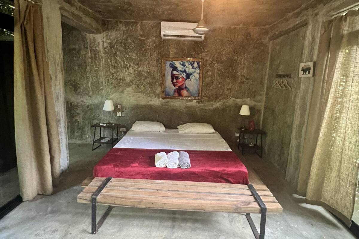 A room with a bed, two bedside tables, a ceiling fan, and a painting on the wall.