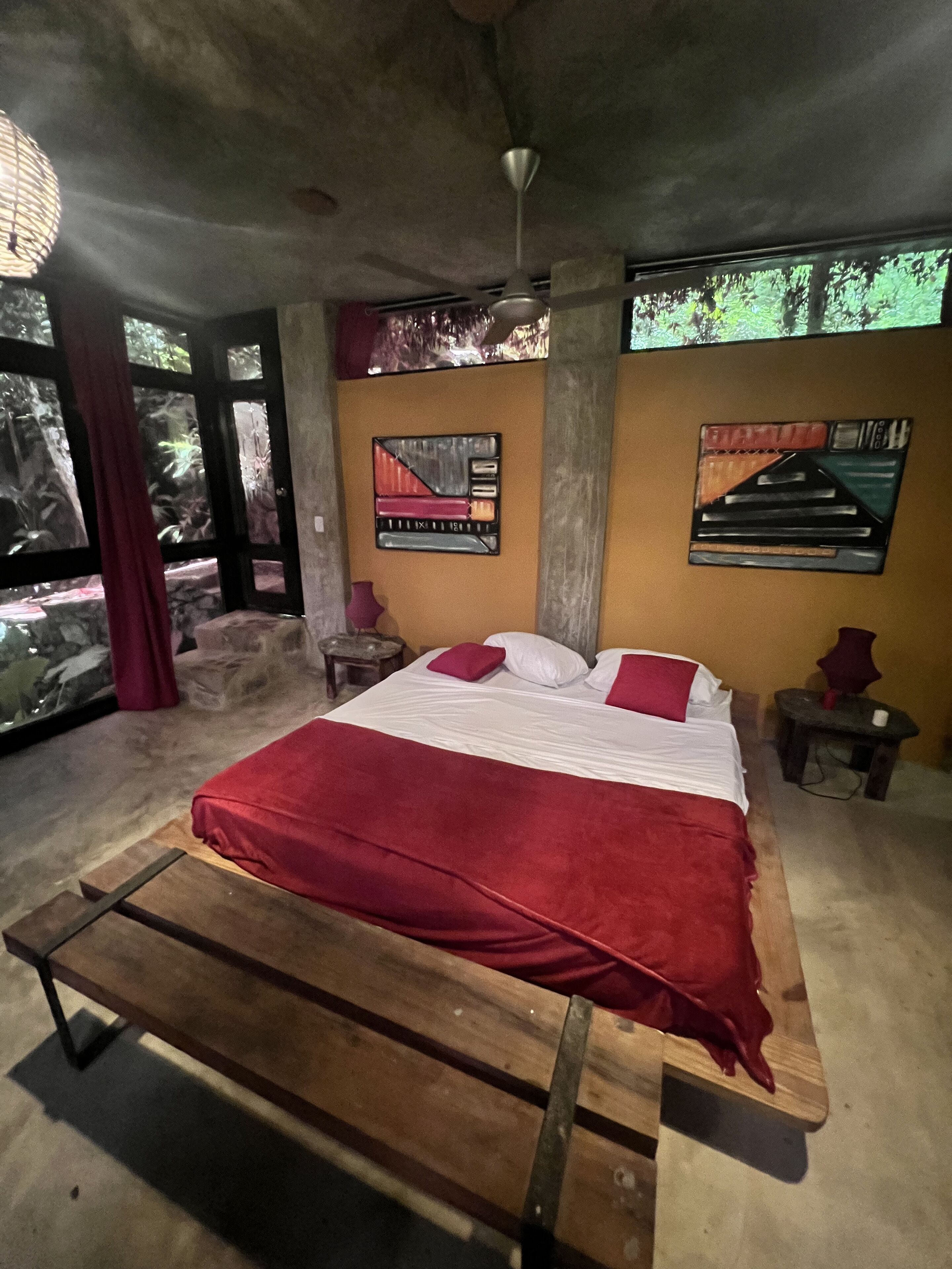 A bedroom with a wooden bed, a red blanket, a ceiling fan, and two wall art pieces.