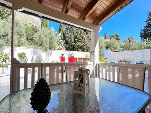 A covered patio with a glass table, a wooden chair, and a decorative pine cone centerpiece.