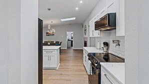 A modern kitchen with white cabinetry, a central island, and a built-in oven. - Heated Saltwater Pool & Spa l Family Friendly l Near Beaches & Clearwater (Palm Harbor)