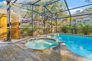 Une piscine avec un jacuzzi, entourée d’une clôture en bois et d’une terrasse en briques.