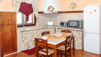 Uma cozinha com mesa de jantar, cadeiras, fogão, micro-ondas e geladeira.