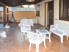 A covered patio area with white plastic furniture, including a sofa and chairs, a small table with a vase, and a decorative turtle statue. - Belvilla by OYO Villa Flora (Mazara del Vallo)