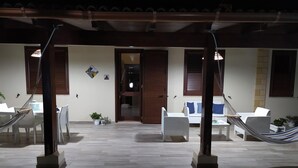Un área de estar al aire libre cubierta con dos hamacas, muebles blancos y plantas en macetas.
