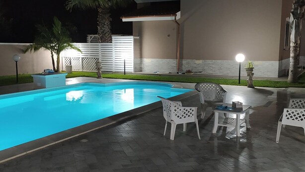 Una piscina con borde de baldosas, rodeada de mobiliario exterior blanco y palmeras.
