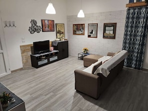 A living room with a TV, sofa, and coffee table, decorated with wall art and a patterned curtain.