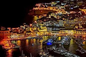Une vue nocturne d’une ville historique densément peuplée, avec des bâtiments le long d’une promenade au bord de l’eau, illuminée par des éclairages artificiels.