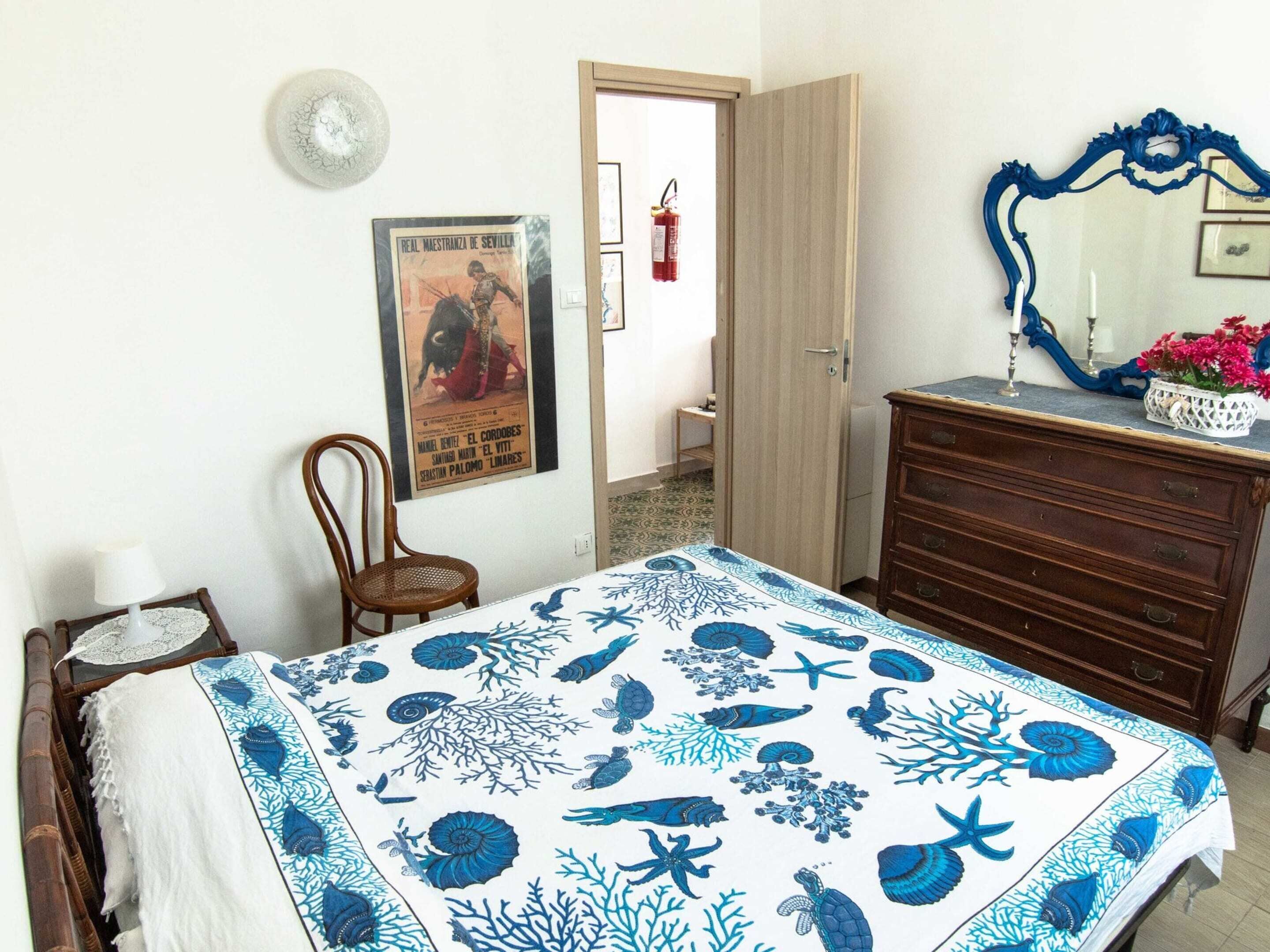 A bedroom with a bed, a dresser, a chair, a poster on the wall, and a door leading to another room.