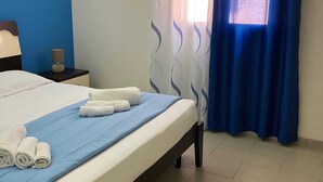 A neatly made bed with blue and white bedding, a bedside lamp, and a window with blue curtains. - Belvilla by Oyo Holiday Home in Ispica (Ispica)