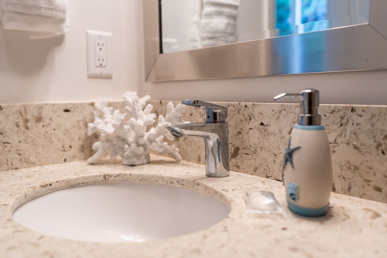 A bathroom with a white sink, a chrome faucet, and a soap dispenser.
