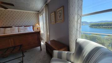 A bedroom with a bed, a nightstand, a dresser, and a view of a lake through a window.
